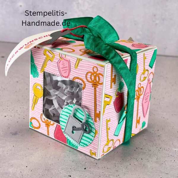 handdekorierte Fensterschachtel mit Glückwunsch-Anhänger, Geschenkbox mit Schlüsselmotiv und grünem Band, Nahaufnahme Fenster der Schachtel mit Füllung, runder Anhänger mit Schloss und Schlüssel, Schachtel geöffnet mit sichtbarem Inhalt, Glückwunsch-Tag an Geschenkbox, Geschenkverpackung für Einzug oder Prüfung